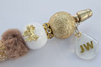 Decorative pen gold and white beads and a fluffy pom-pom on a light gray background. with JW charm