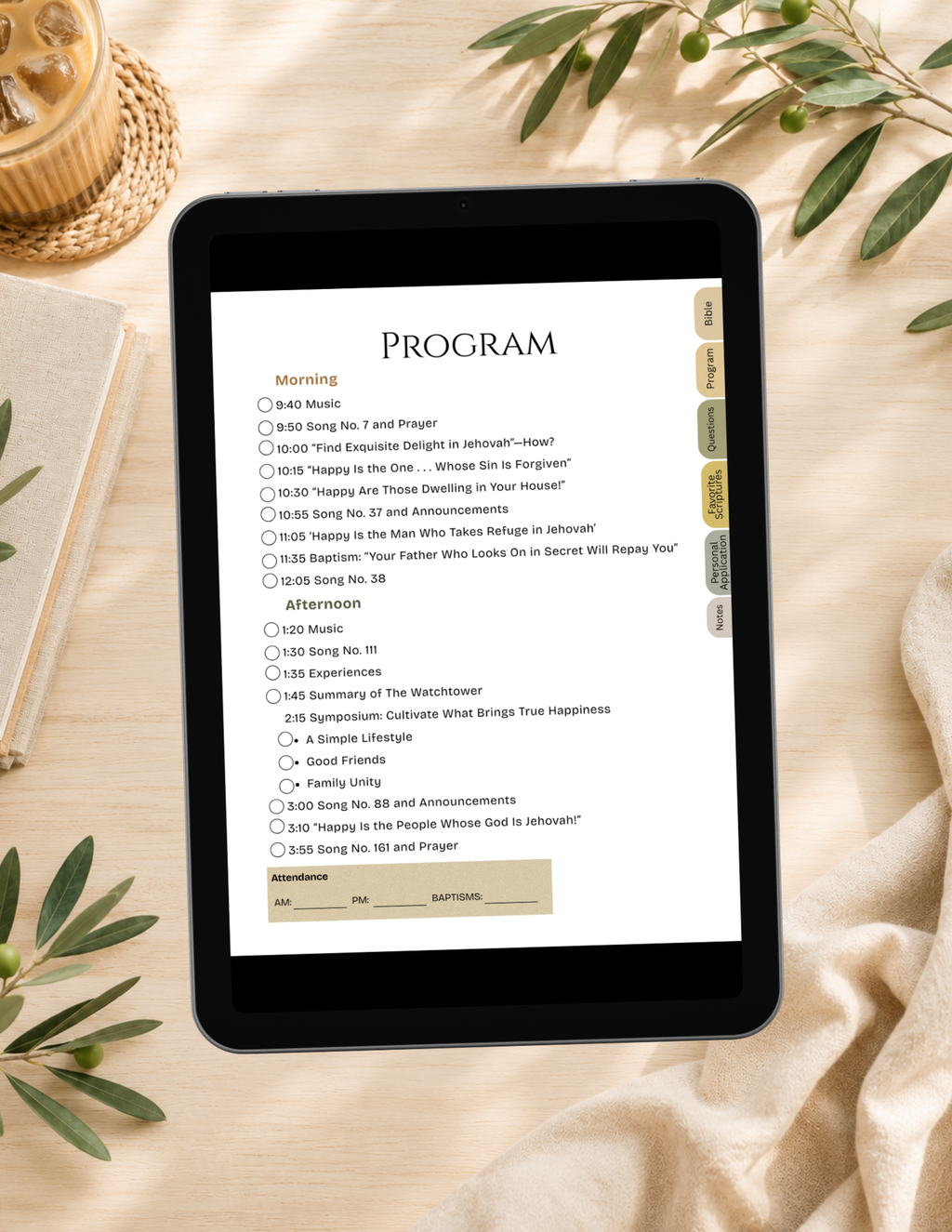 A tablet device displaying a digital program or checklist interface, placed on a beige fabric surface with decorative leaves, a woven basket, and a candle visible around it.
