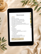 A tablet device displaying a digital program or checklist interface, placed on a beige fabric surface with decorative leaves, a woven basket, and a candle visible around it.