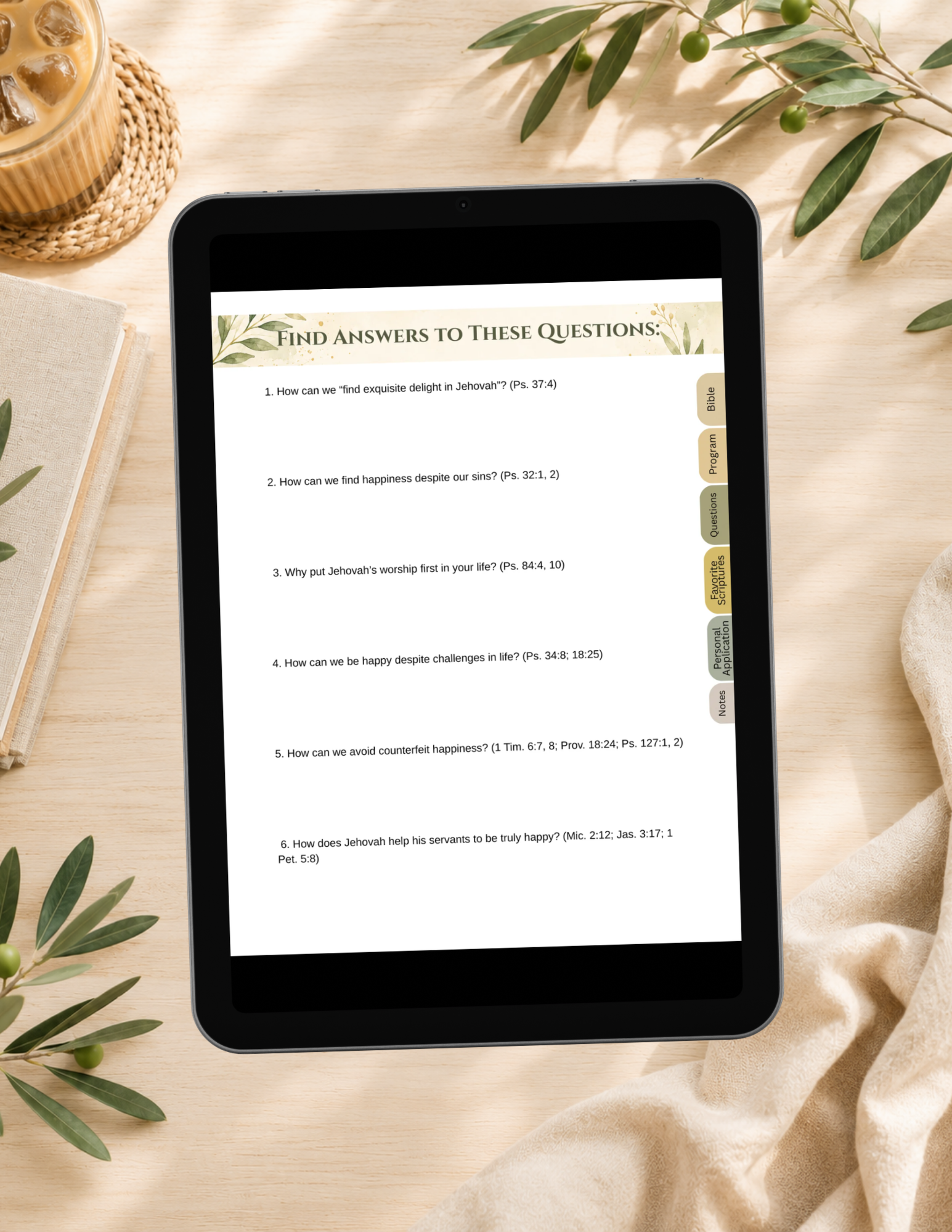 A tablet device lying on a beige fabric surface, displaying a Bible study worksheet titled 'FIND ANSWERS TO THESE QUESTIONS' with scripture questions and answers. The scene is styled with olive branches, a woven coaster, a candle, and a notebook.