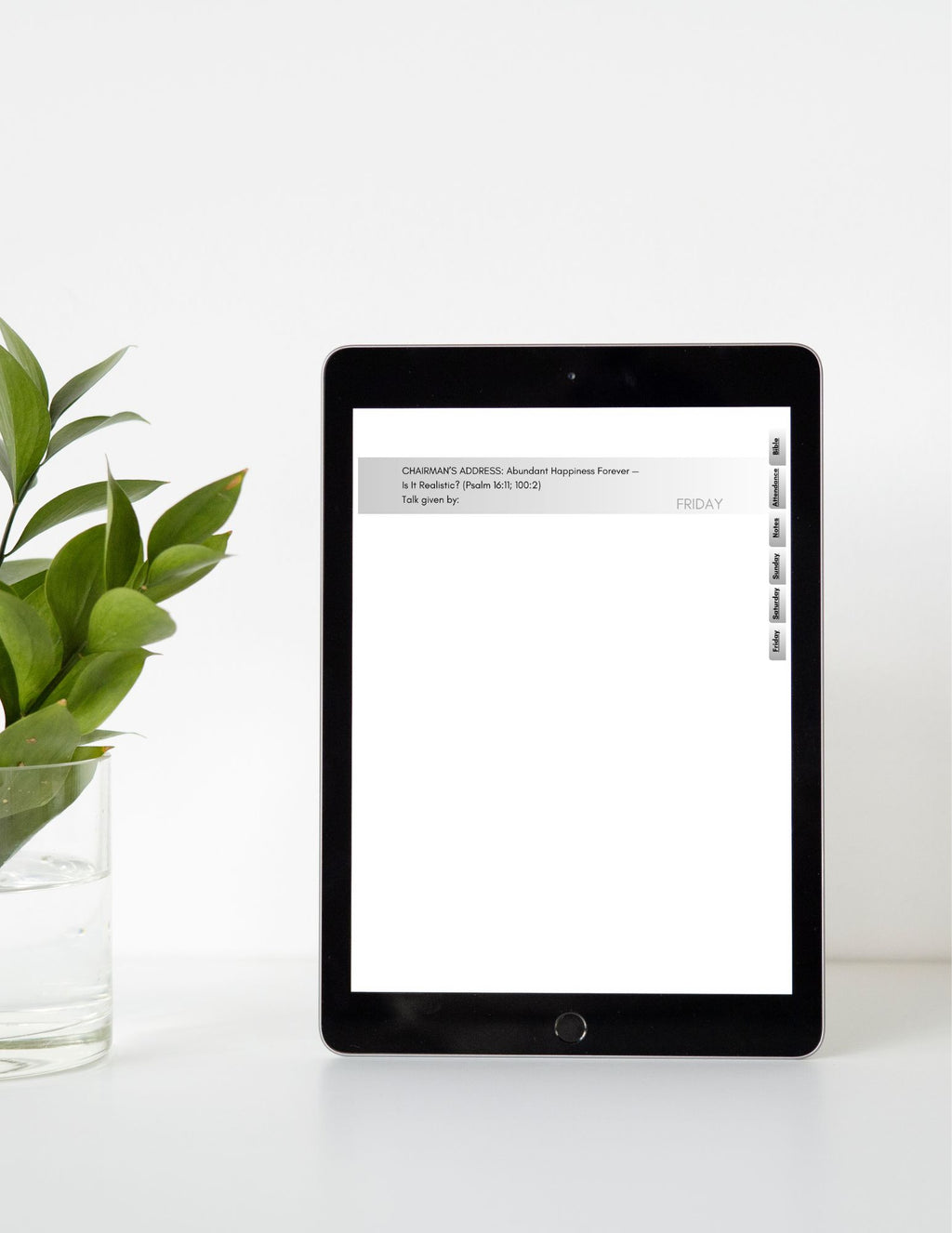 Tablet with a white screen displaying text on a white surface with a green plant.