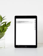 Tablet with a white screen displaying text on a white surface with a green plant.