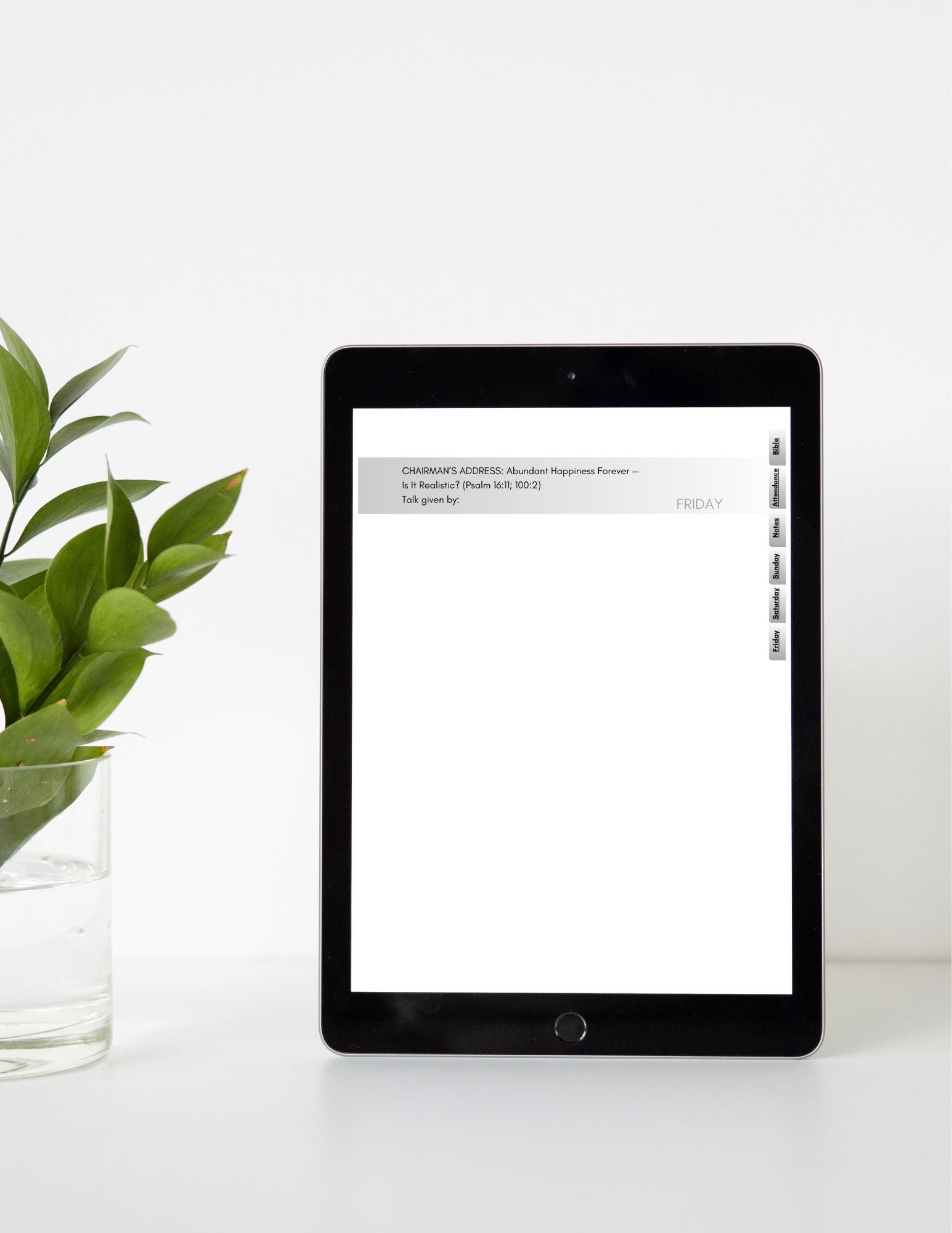 Tablet with a white screen displaying text on a white surface with a green plant.