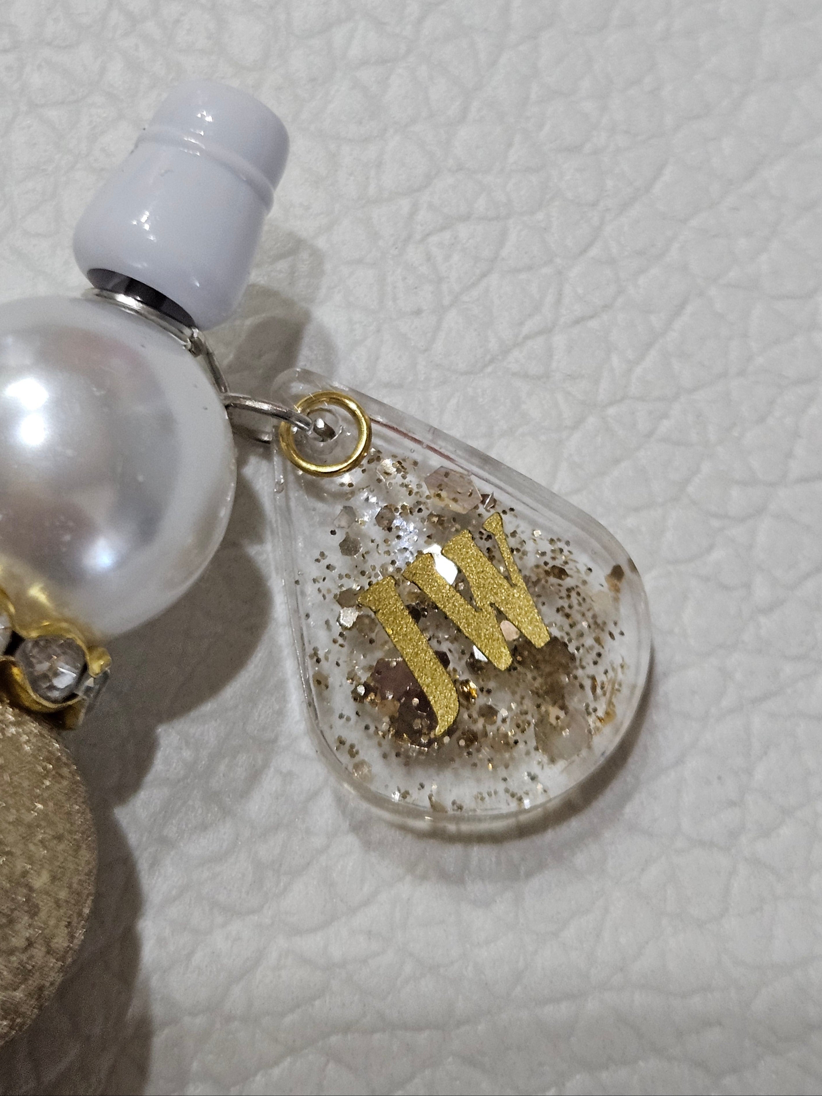 Close-up of a clear teardrop-shaped charm with gold lettering on a textured white background