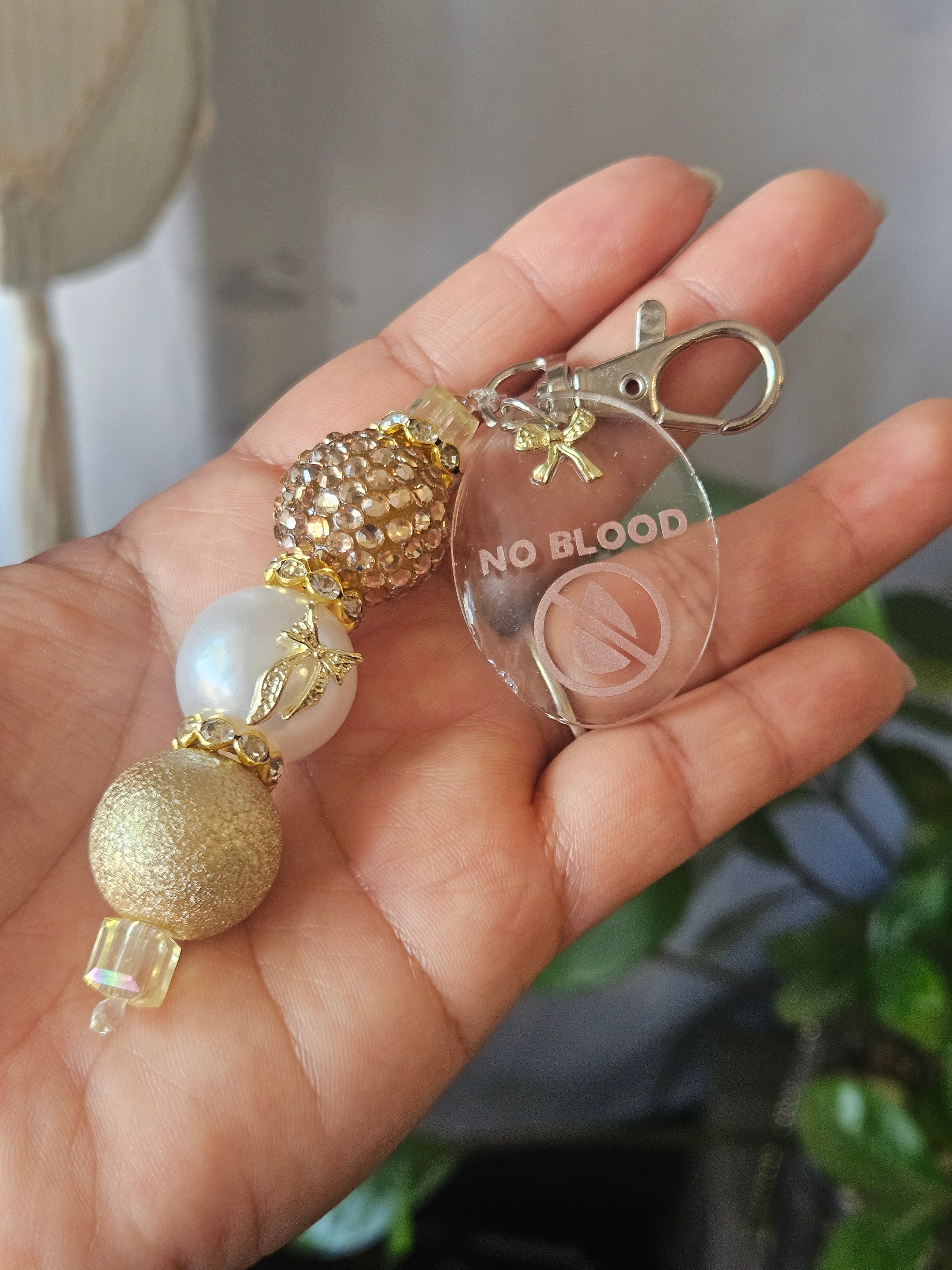 Hand holding a keychain with decorative beads and 'No Blood' tag.