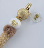 Decorative JW pen with gold and white beads and a charm on a light gray background