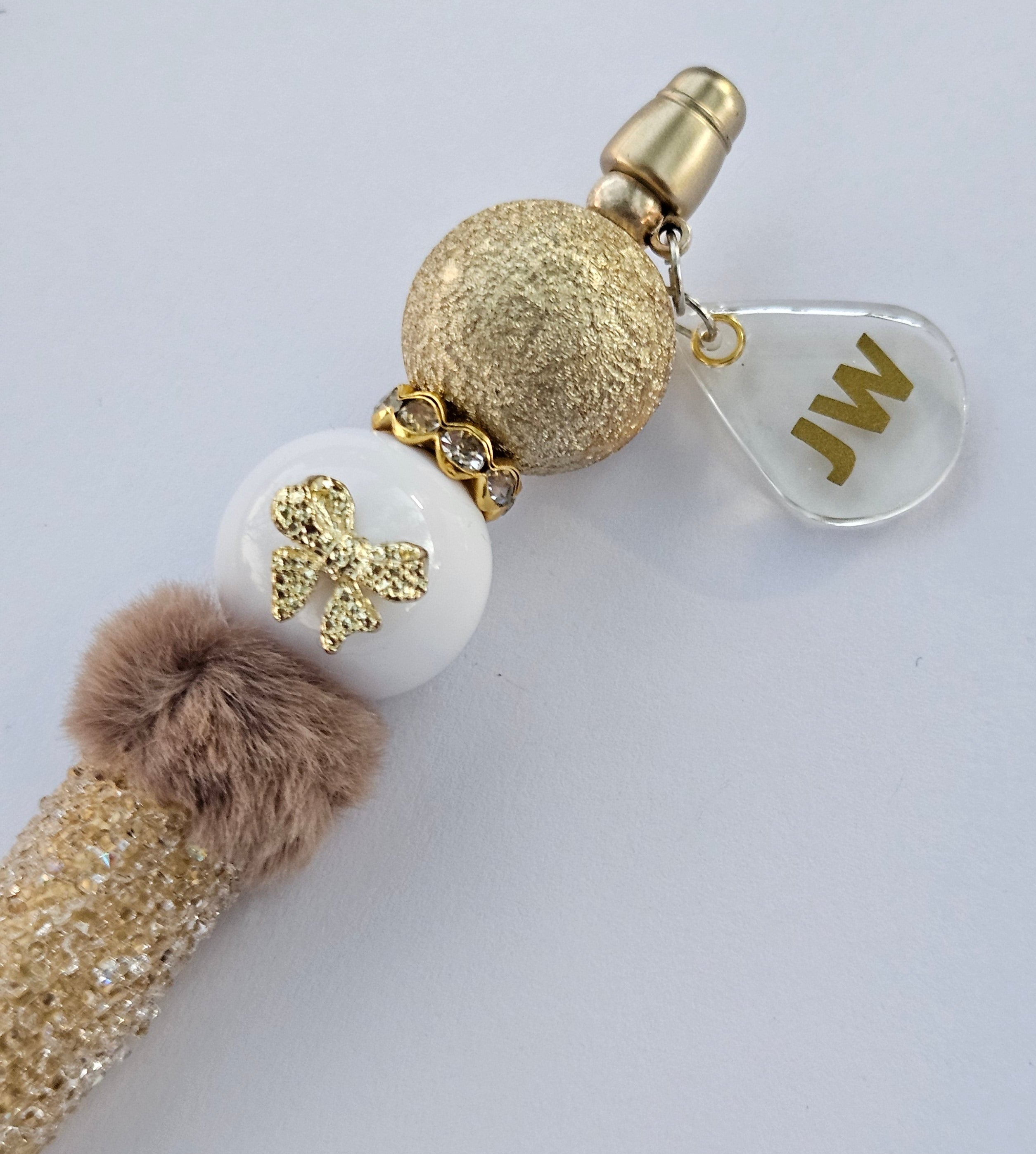 Decorative JW pen with gold and white beads and a charm on a light gray background