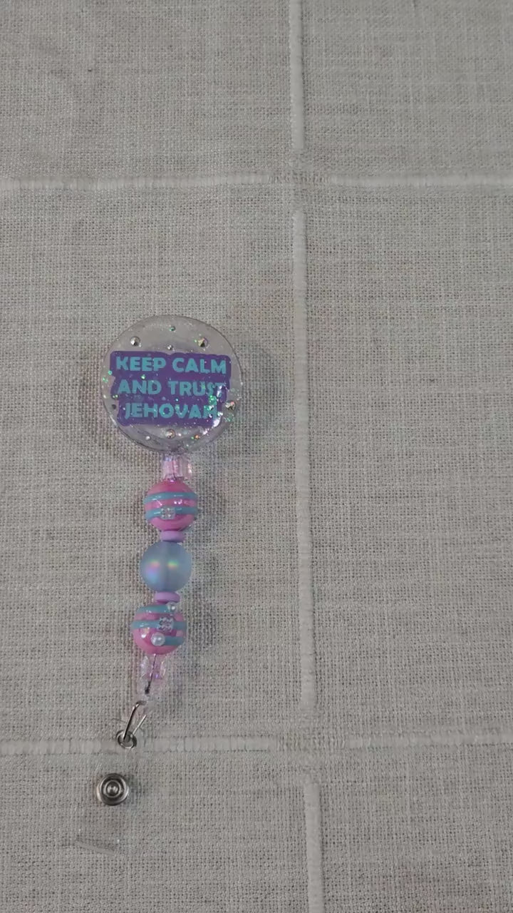 Hand-poured circle-shaped glitter resin badge reel with “Keep Calm and Trust Jehovah” message, iridescent glitter and pink & blue accent beads, for JW pioneers video